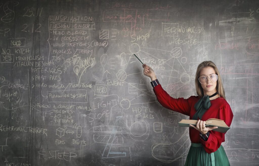 strict female teacher with book pointing at scribbled blackboard